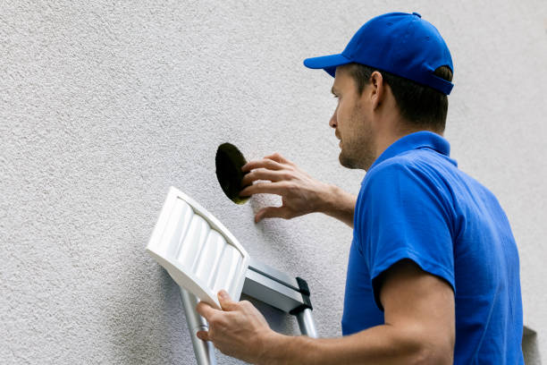 man in blue uniform standing on ladder outdoors and doing maintenance for house ventilation system